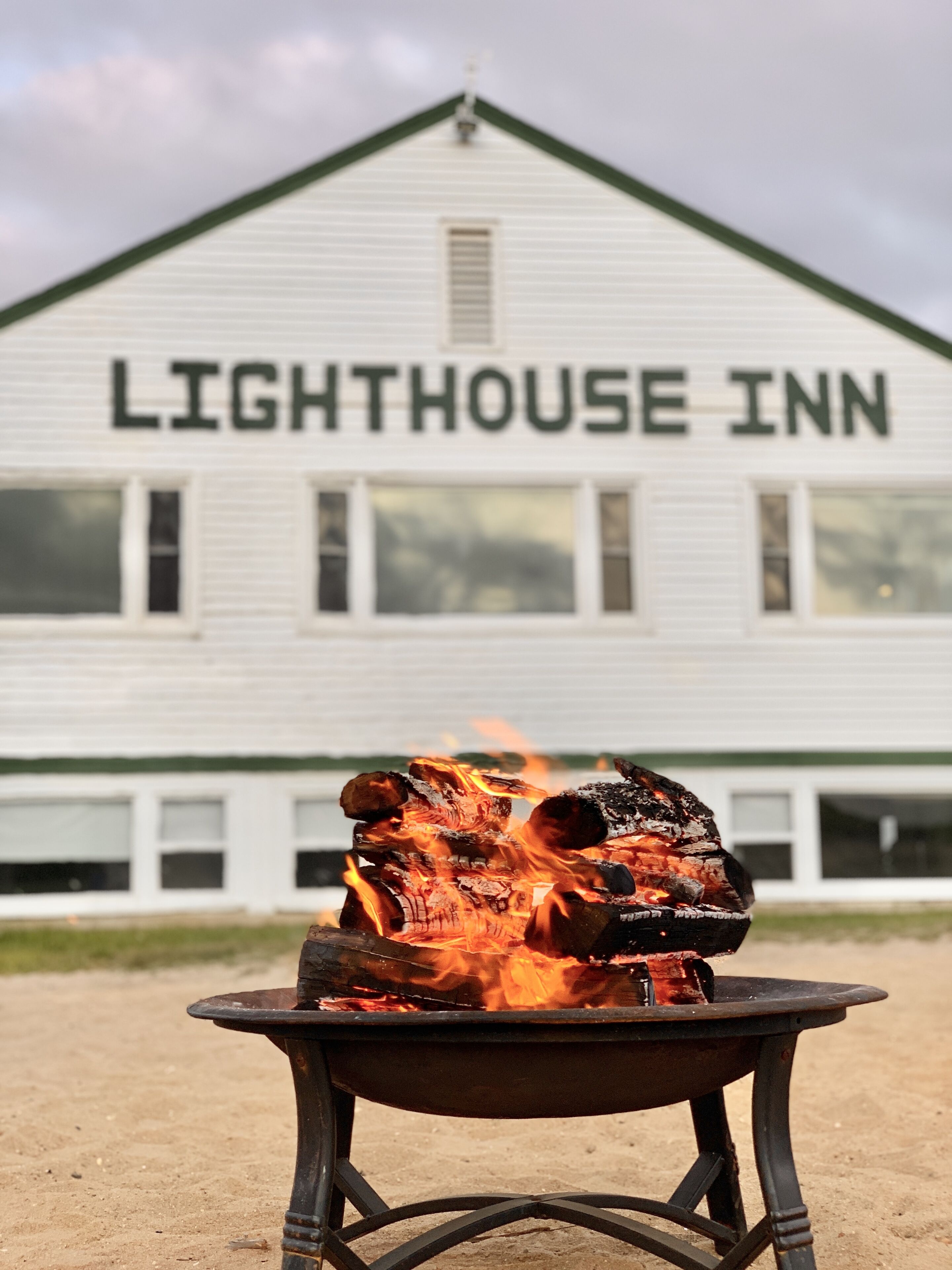 A fire pit with burning logs in front of a building labeled "Lighthouse Inn".