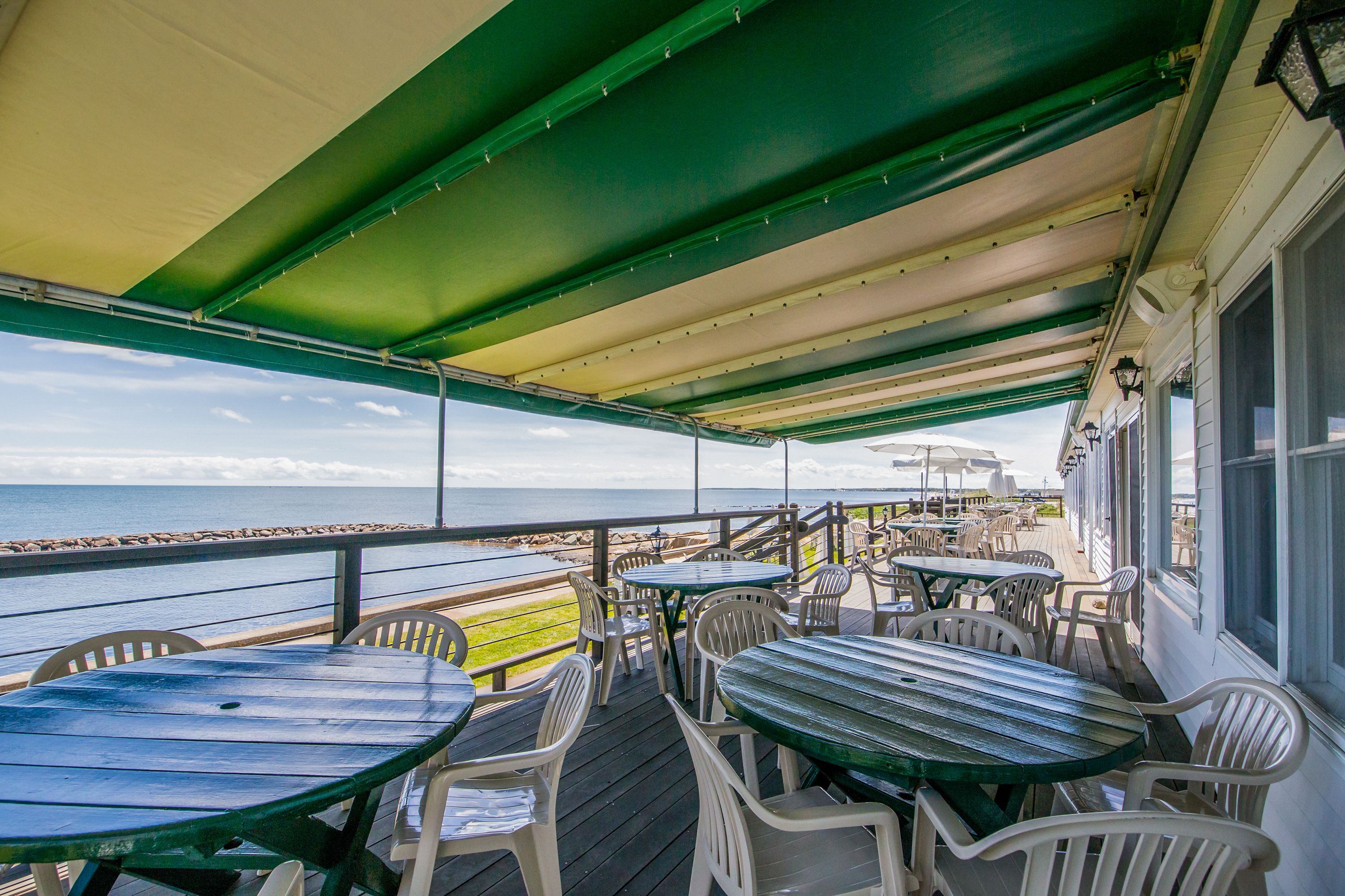 A covered outdoor seating area with tables and chairs, overlooking the ocean.