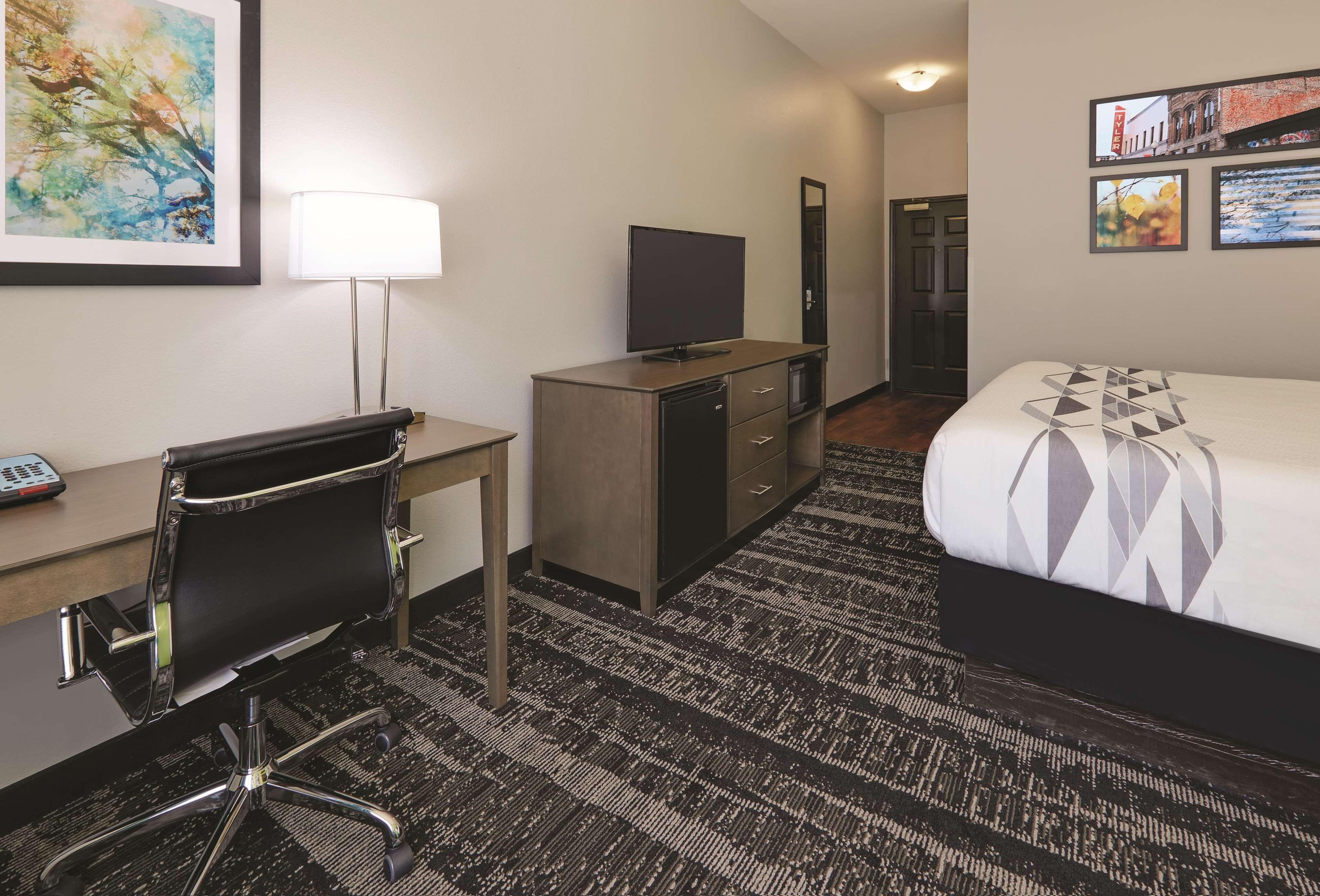 A hotel room with a bed, desk, chair, TV, and artwork on the walls.