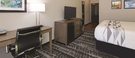 A hotel room with a bed, desk, chair, TV, and artwork on the walls.