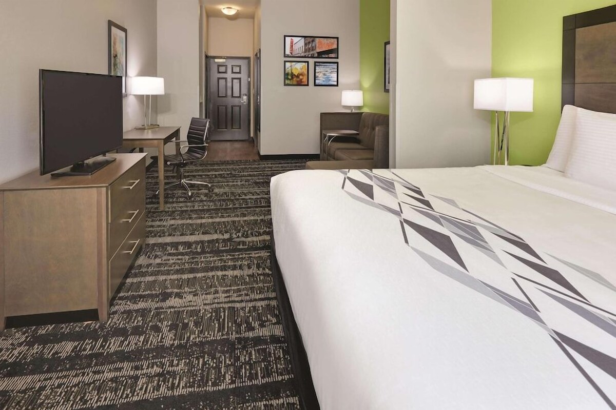 A hotel room with a bed, a desk with a TV, a chair, a lamp, and a carpeted floor.