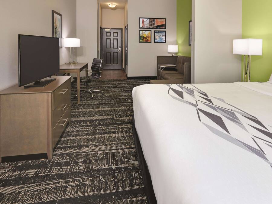 Quarto de hotel com uma cama grande, uma escrivaninha com um computador, uma cadeira, uma televisão e um abajur.