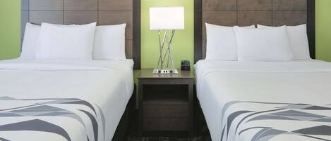 A hotel room with two beds, a nightstand with a lamp, and a patterned rug.