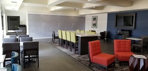 A modern conference room with a large table, several chairs, a projector screen, and a television.