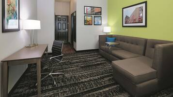 A hotel room with a sofa, a desk, a chair, a lamp, and a framed picture on the wall.