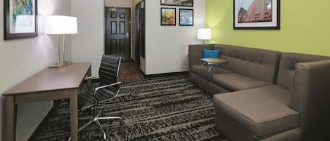 A hotel room with a sofa, a desk, a chair, a lamp, and a framed picture on the wall.