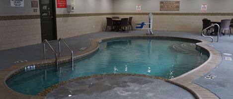 An indoor swimming pool with safety warnings, a door, and seating areas.