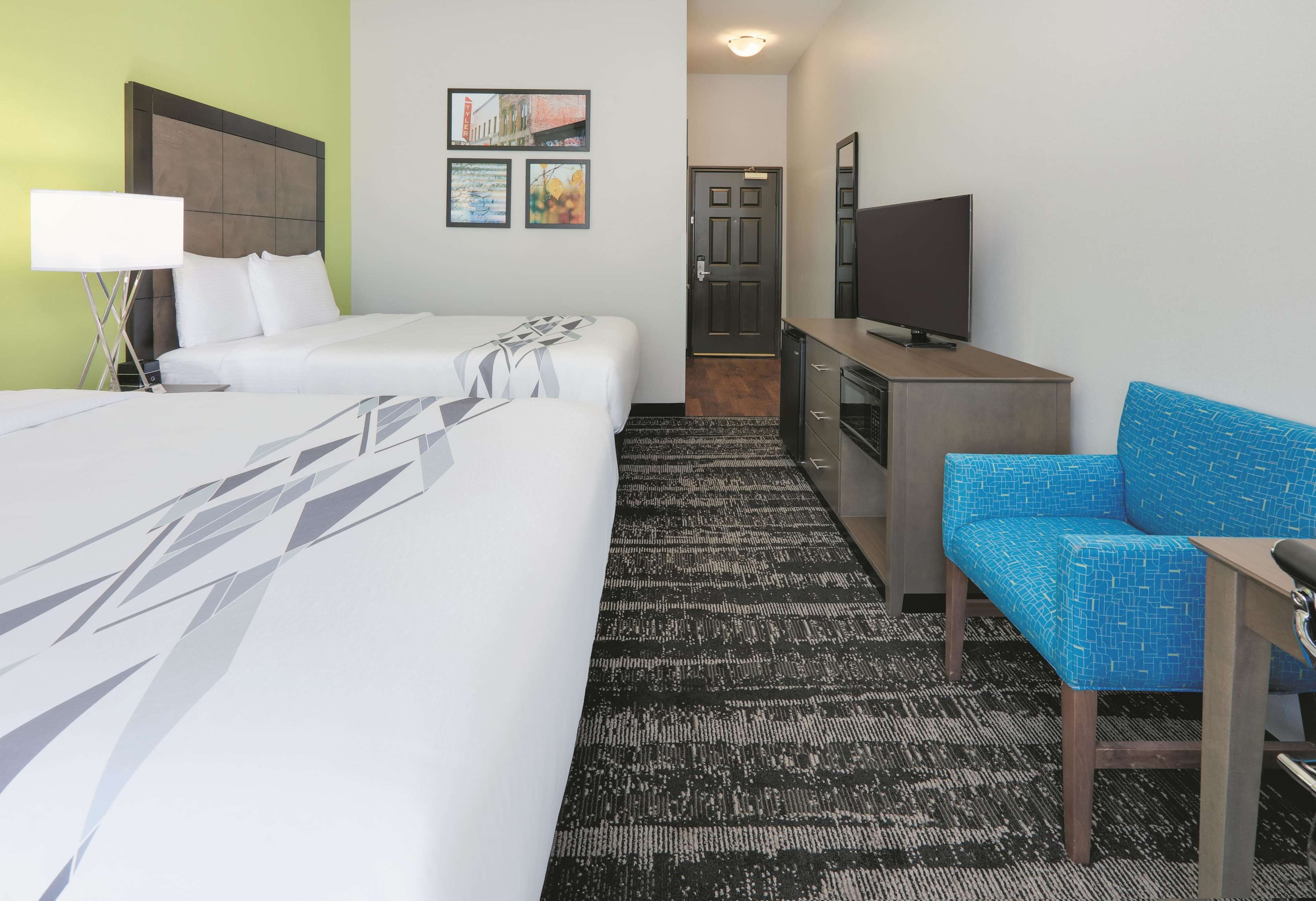 A hotel room with two beds, a television, a desk, and a blue chair.