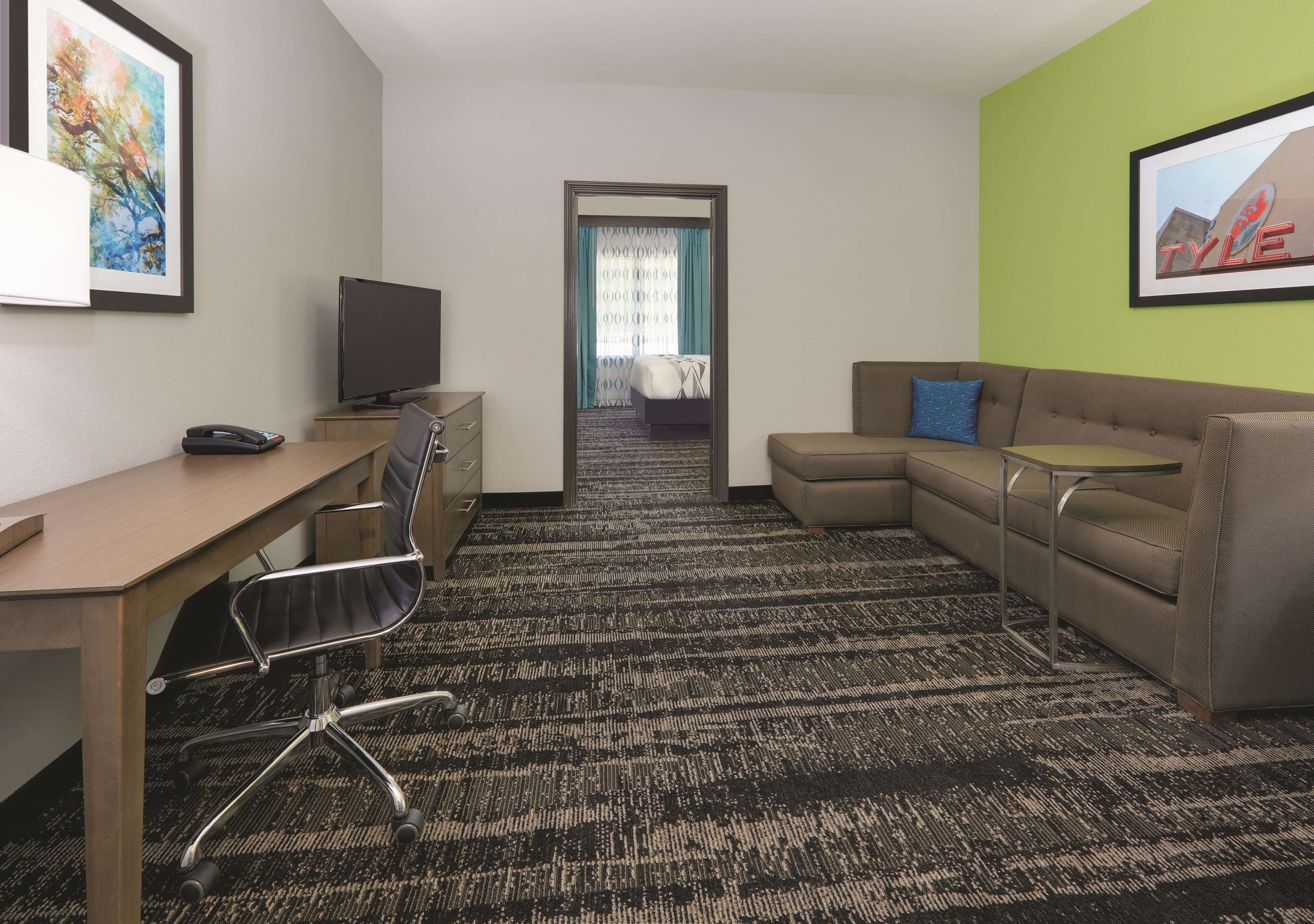 A hotel room with a desk, a sofa, a television, and a carpeted floor.