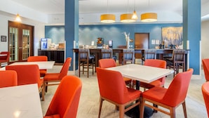 A modern dining area with red chairs and white tables, featuring a blue accent wall and a reception desk with a coffee machine. - Comfort Inn & Suites Brighton Denver NE Medical Center (Brighton)