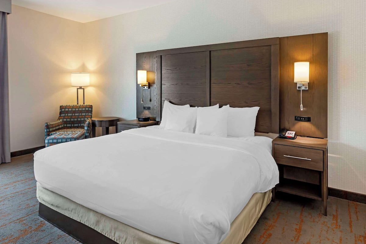 A hotel room with a large bed, two bedside tables, a chair, and two wall-mounted lamps.