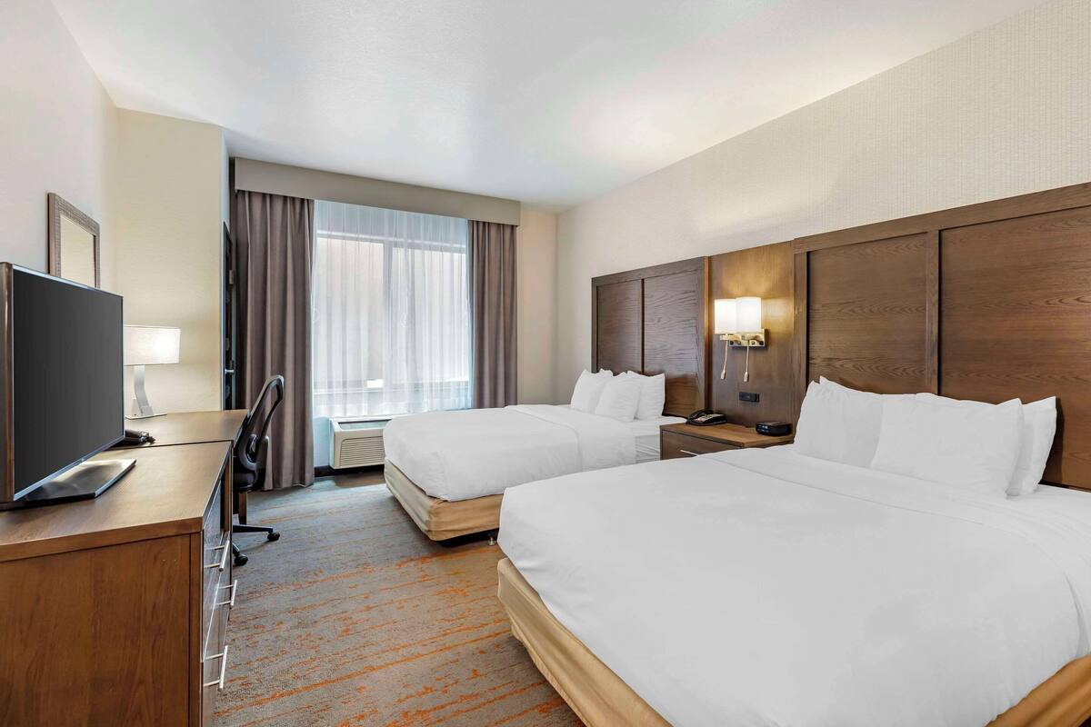 A hotel room with two beds, a desk with a TV, a chair, a lamp, and a window with curtains.