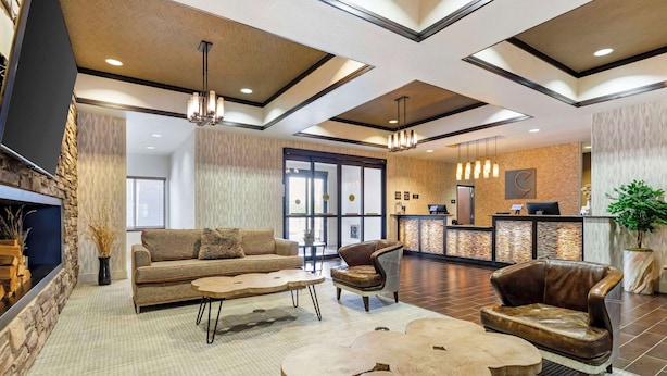 A modern lobby with a sofa, armchair, and coffee table, a reception desk, and a large window. - Comfort Inn & Suites Brighton Denver NE Medical Center (Brighton)