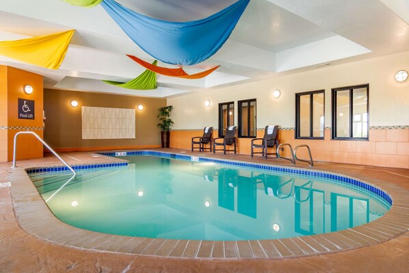 An indoor swimming pool with a blue tiled edge, a pool lift, and a seating area with chairs. - Comfort Inn & Suites Brighton Denver NE Medical Center (Brighton)