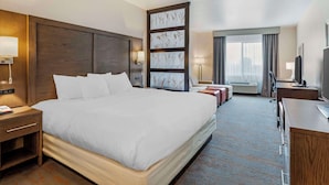 A hotel room with a large bed, a desk, a chair, a TV, and a window with curtains. - Comfort Inn & Suites Brighton Denver NE Medical Center (Brighton)