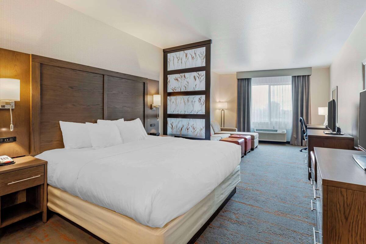 A hotel room with a large bed, a desk, a chair, a TV, and a window with curtains.