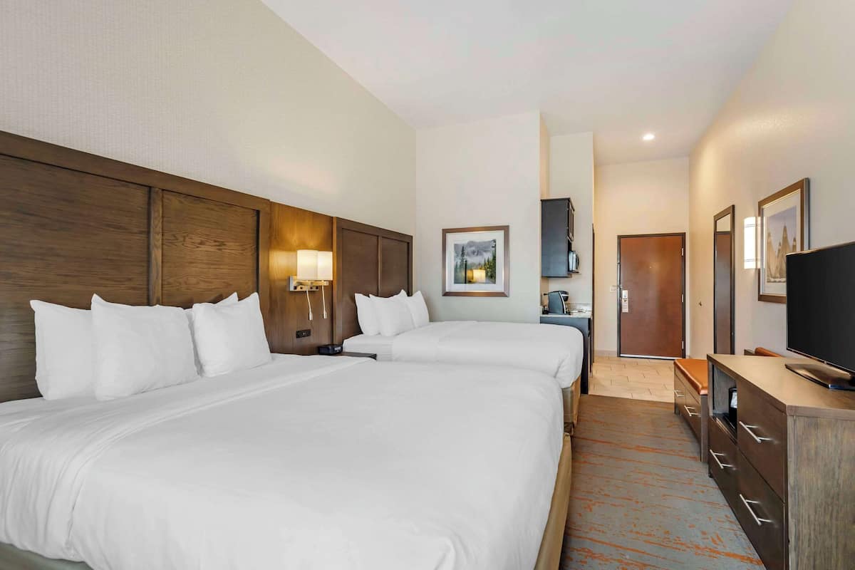 A hotel room with two beds, a desk, a television, and a door leading to a bathroom.