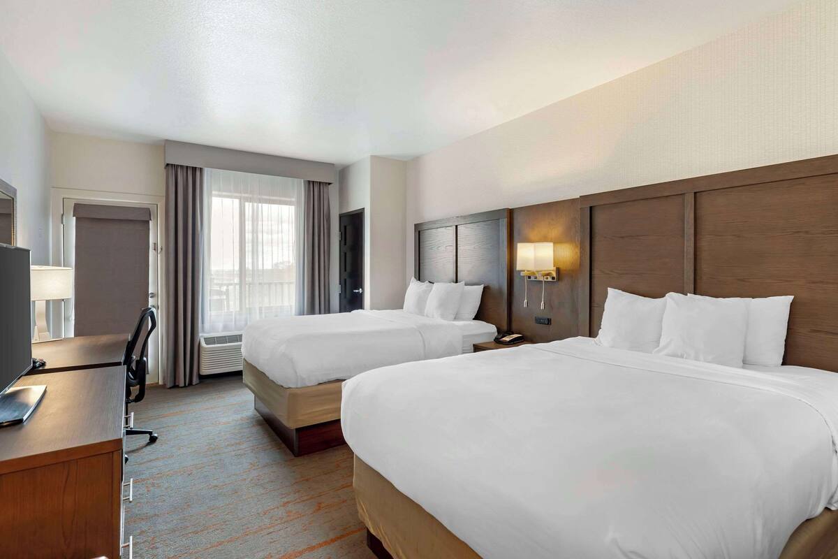 A hotel room with two beds, a desk, a TV, and a window with curtains.