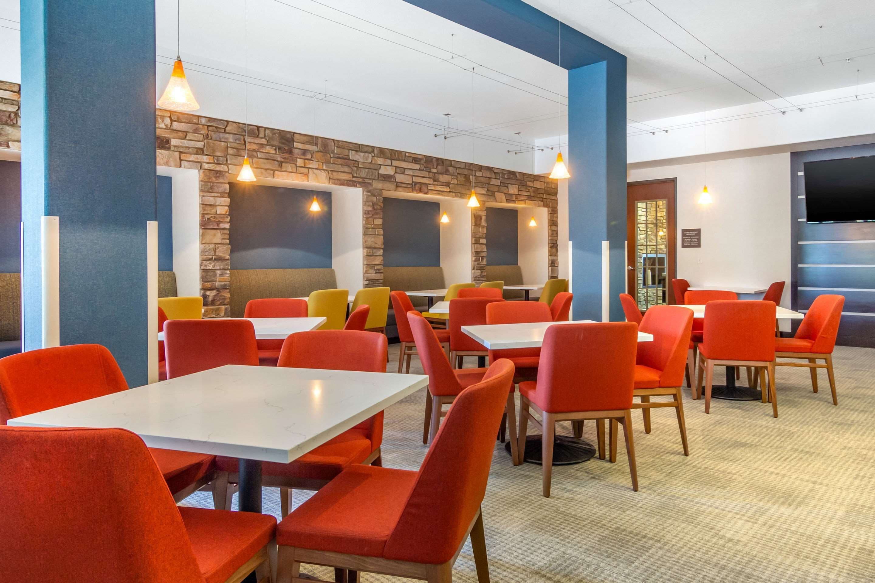 A restaurant with red and yellow chairs, white tables, and a stone wall.