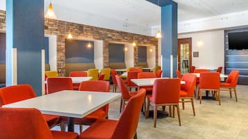 A restaurant with red and yellow chairs, white tables, and a stone wall.