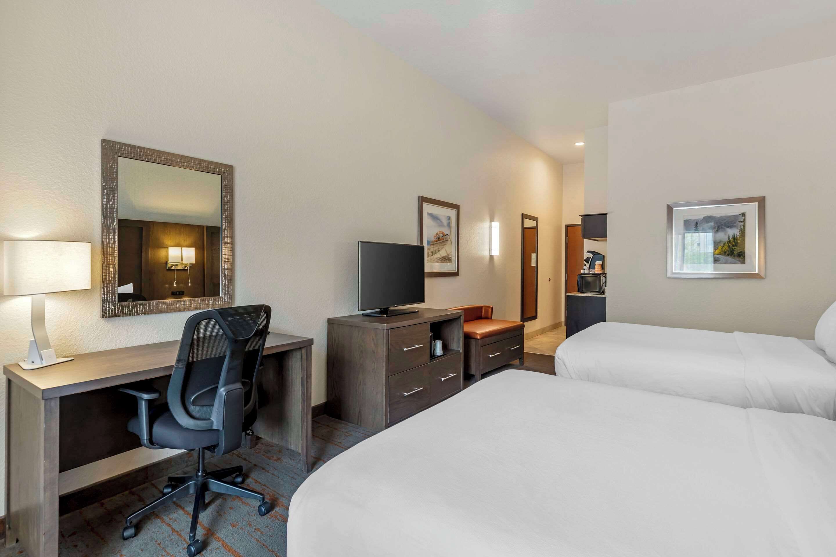 A hotel room with a desk, chair, TV, and two beds.