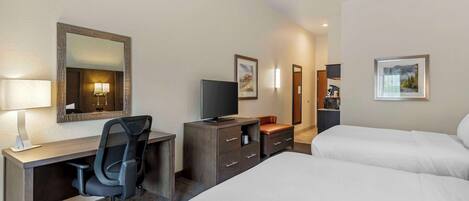 A hotel room with a desk, chair, TV, and two beds.