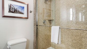 A bathroom with a framed picture of a building, a toilet, a glass shower enclosure, and a towel rack.