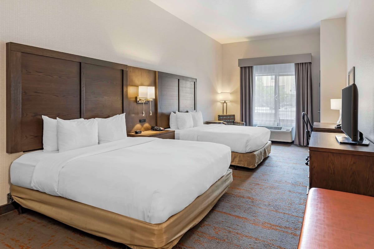 A hotel room with two beds, a desk, a TV, and a window with curtains.
