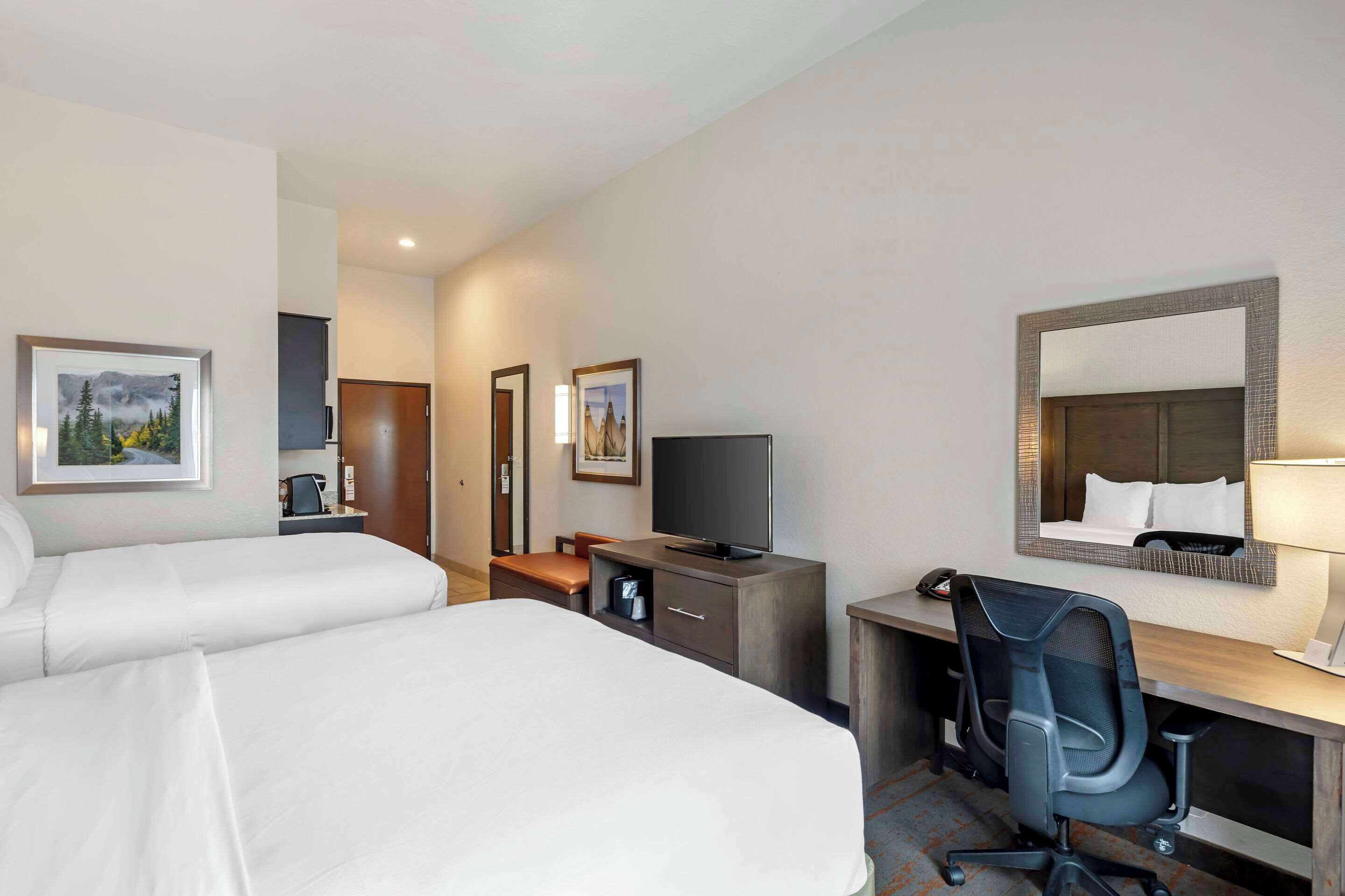 A hotel room with two beds, a desk, a chair, a TV, and a mirror.