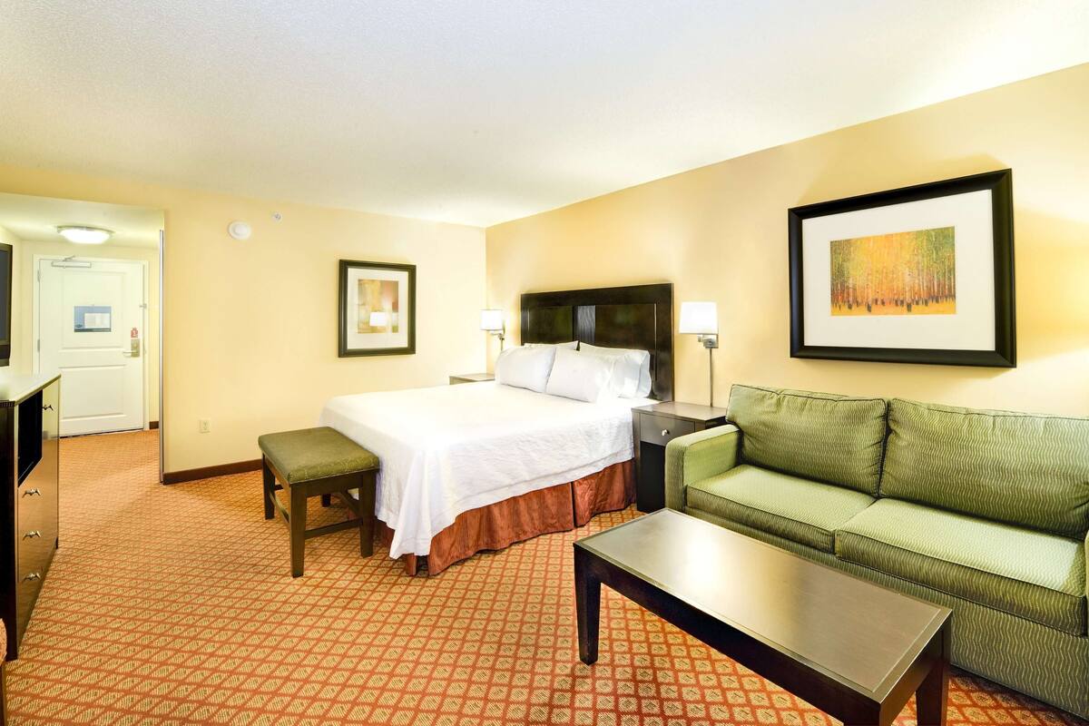 A hotel room with a bed, a green sofa, a coffee table, a TV, and a desk.