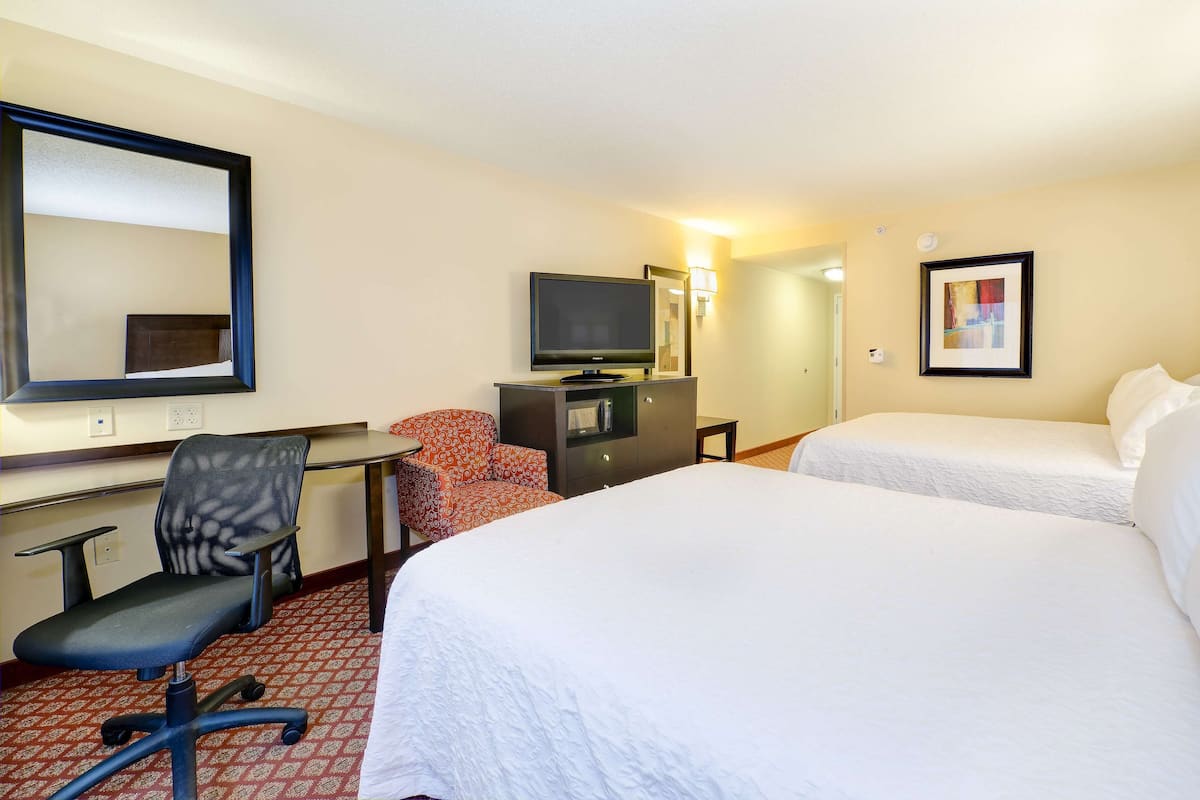 A hotel room with two beds, a desk with a chair, a television, and a mirror.