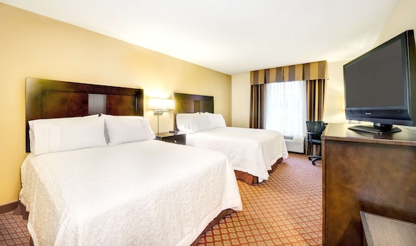 A hotel room with two beds, a desk with a television, and a window with curtains.