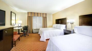 A hotel room with two beds, a desk, a chair, a TV, and a window with curtains.