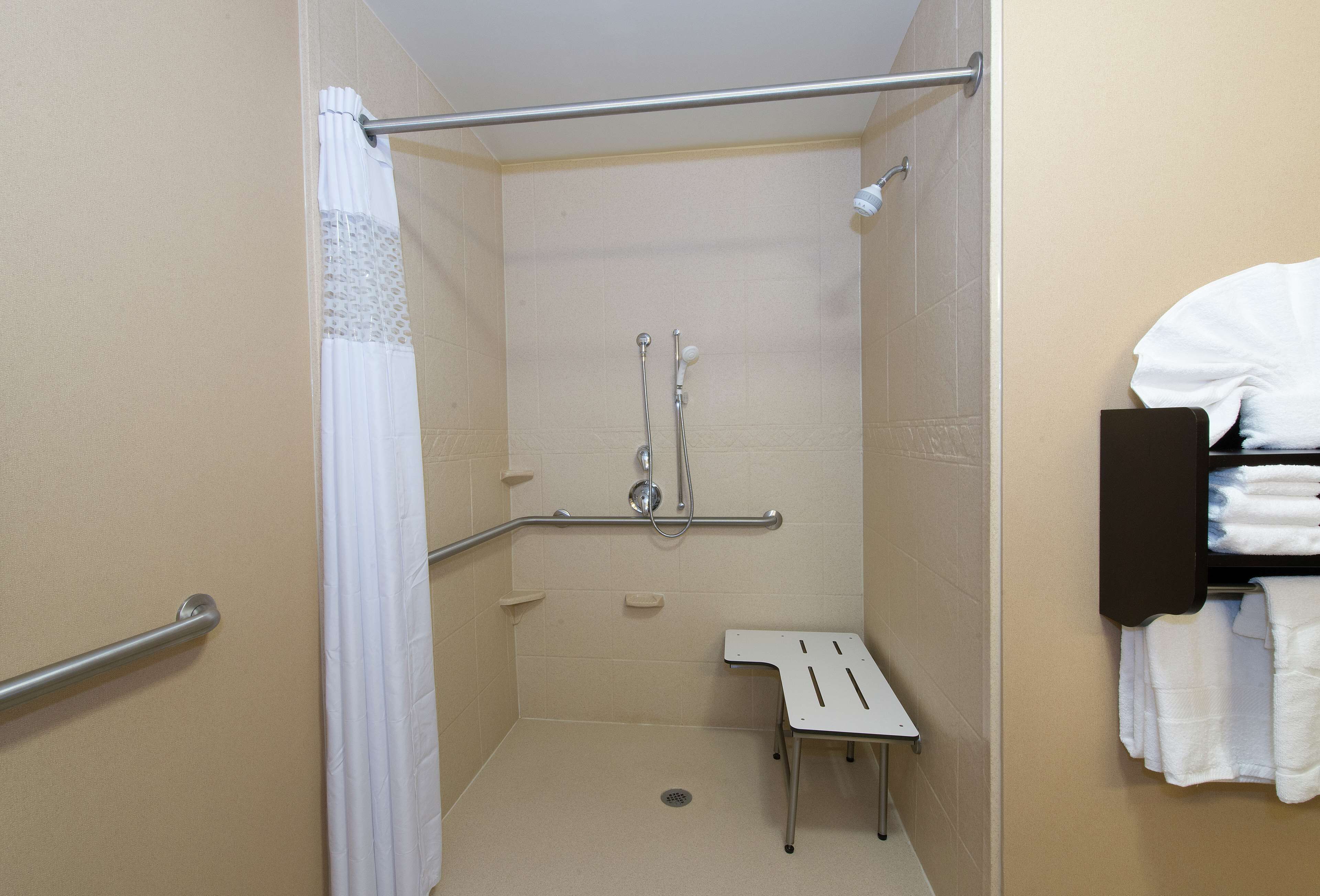 A small, enclosed shower area with a grab bar, a bench, and a towel rack.