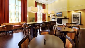 A hotel lobby with a sofa, dining tables, chairs, a bar area, and a fireplace. - Hampton Inn Suites Scottsboro (Scottsboro)