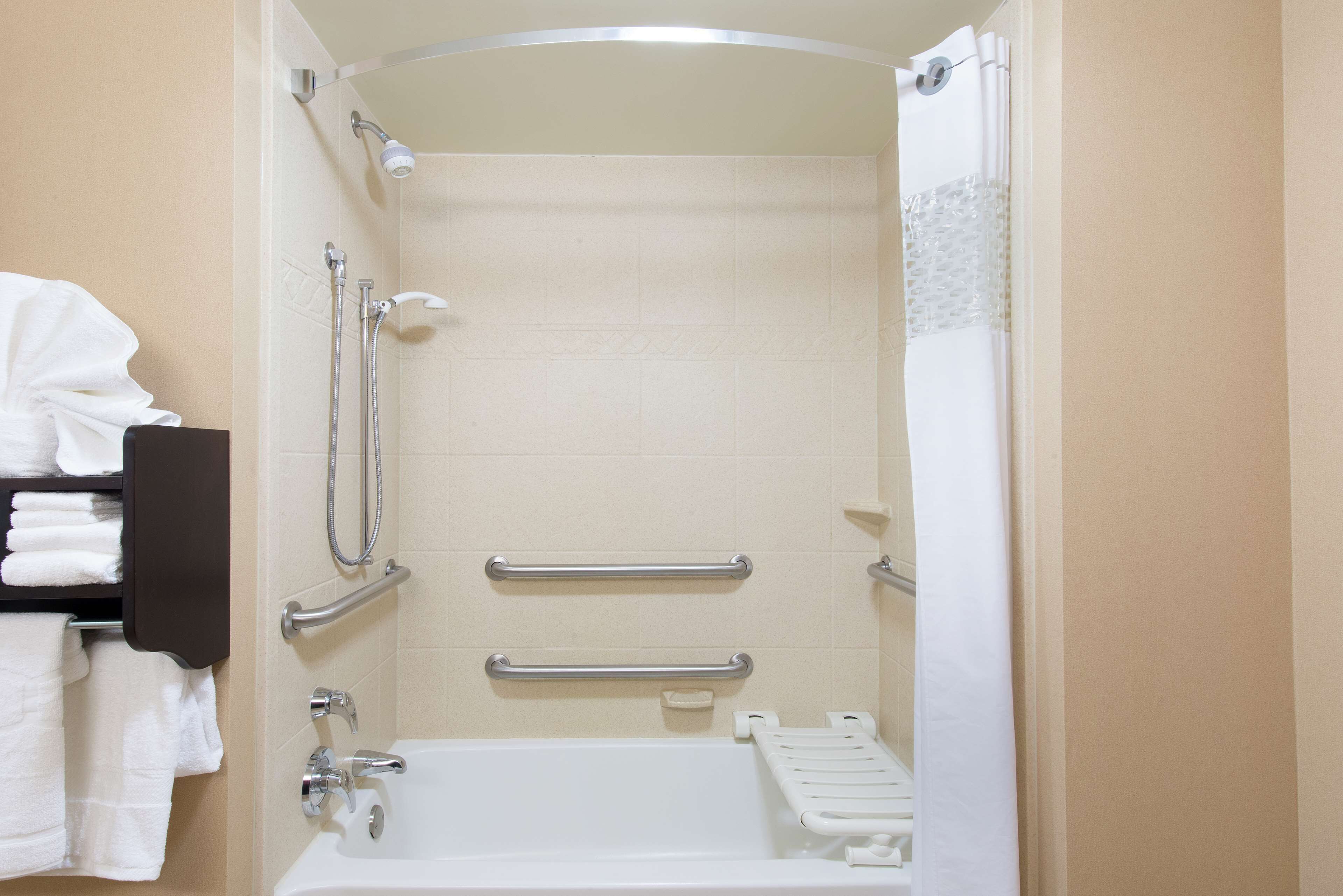 A bathroom with a bathtub, grab bars, a showerhead, and a towel rack.