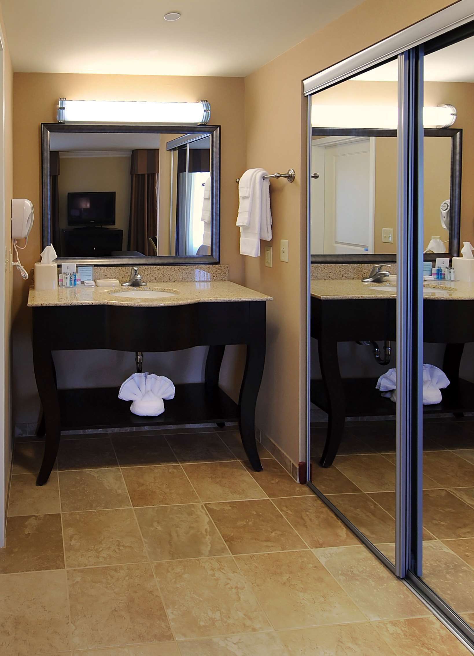 A bathroom with two sinks, a large mirror, a towel rack, and a shower area.