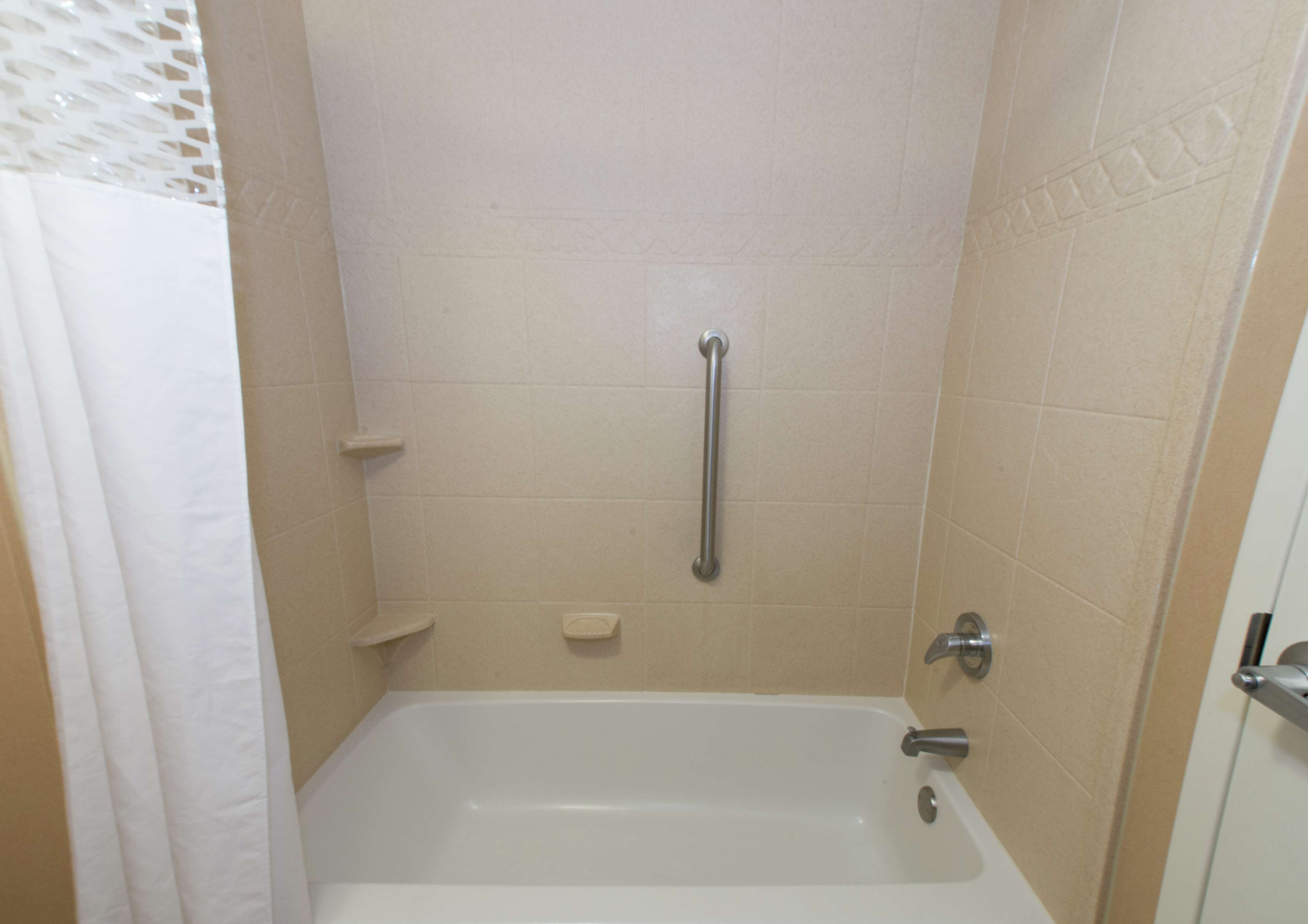 Un baño con bañera, ducha con barra de apoyo y retrete.