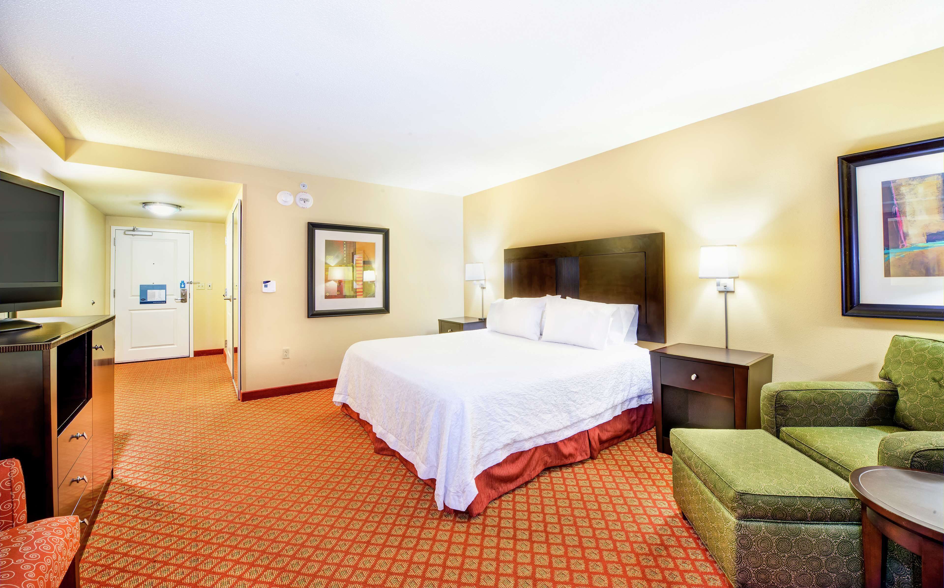 Een hotelkamer met een groot bed, een bureau met een televisie, een stoel, een bank en een lijst met een afbeelding aan de muur.