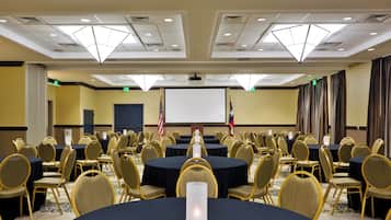 Un salón de conferencias con varias mesas y sillas, una pantalla de proyector y banderas.