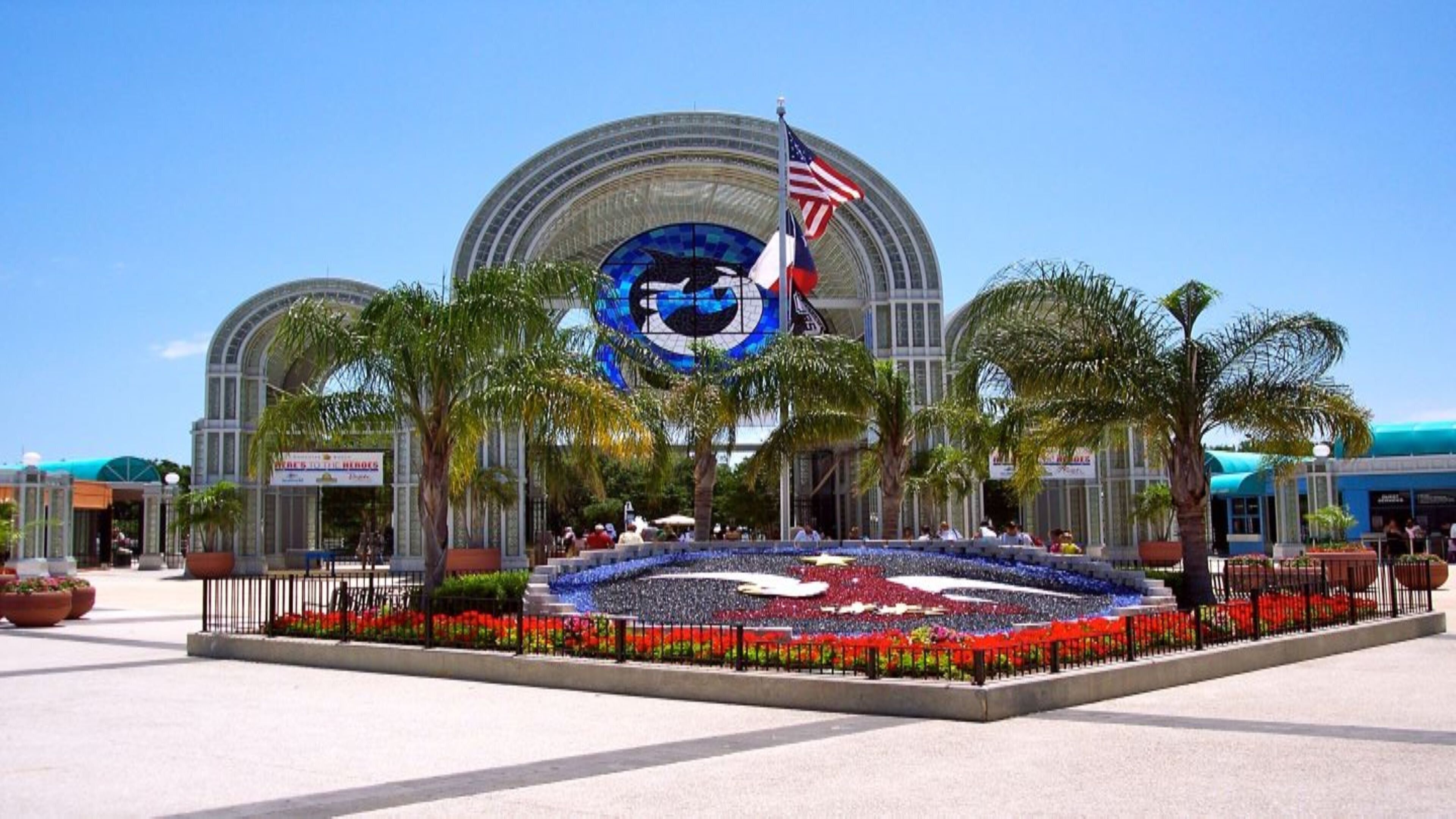 Un grand bâtiment à la forme circulaire, surmonté d’un drapeau et doté d’une fontaine centrale agrémentée de fleurs aux couleurs vives.