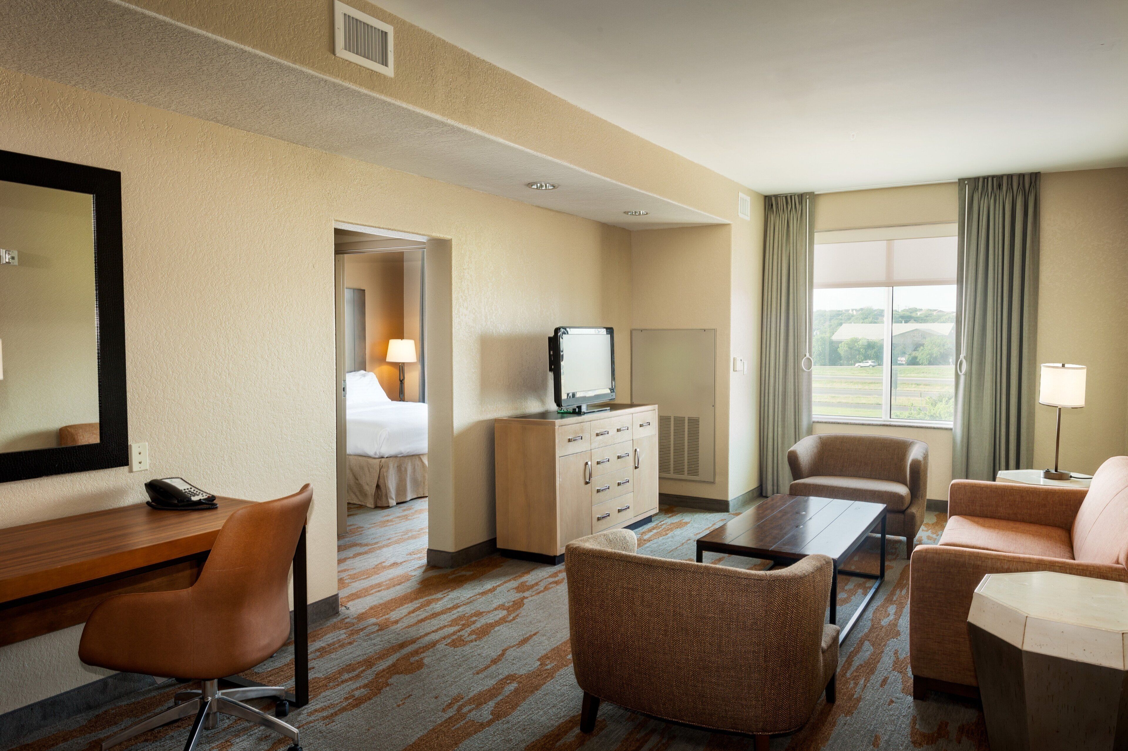 A hotel room with a bed, a desk with a telephone, a television, a sofa, a chair, and a large window with curtains.