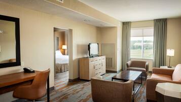 A hotel room with a bed, a desk with a telephone, a television, a sofa, a chair, and a large window with curtains.