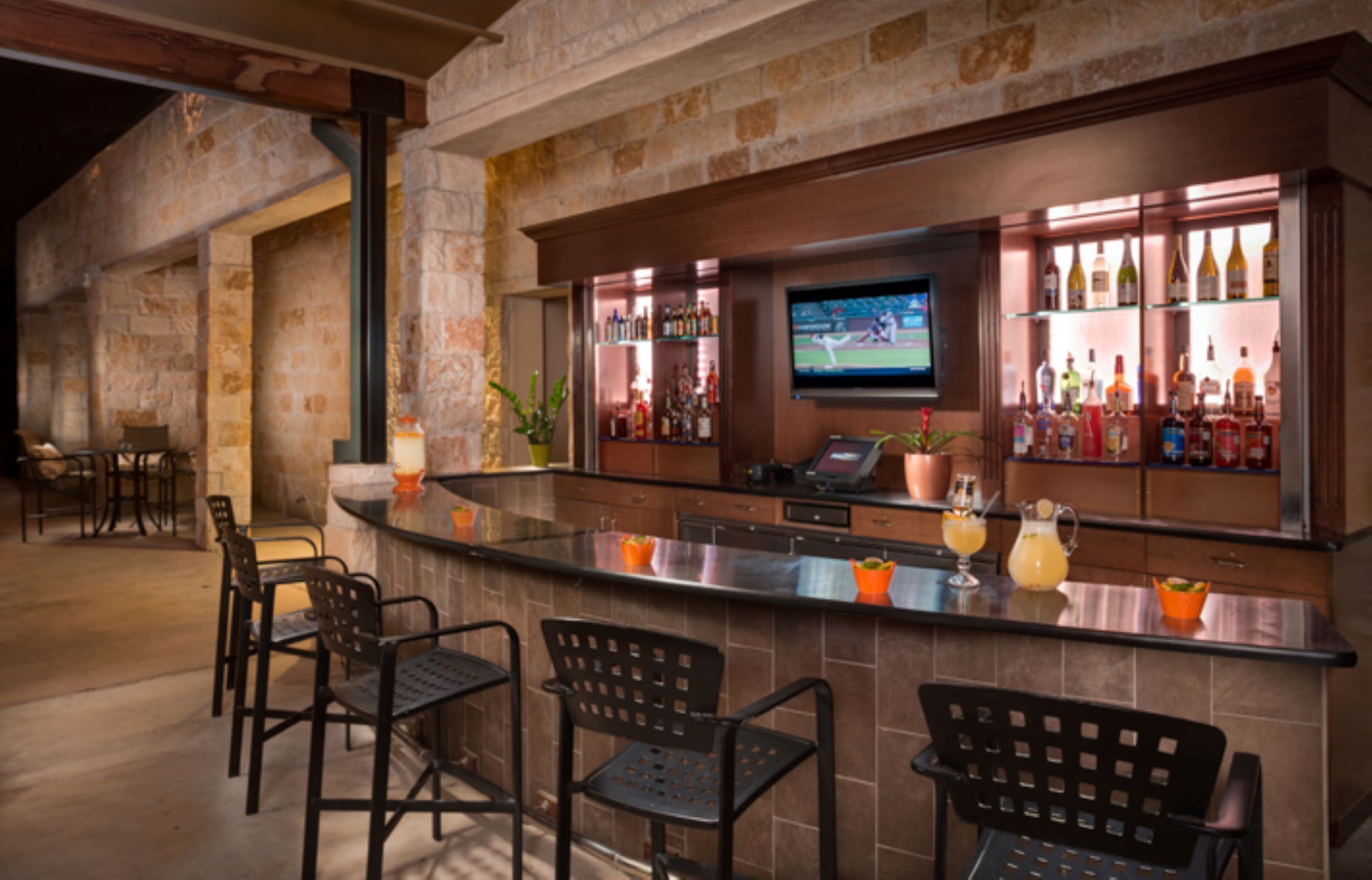 Zona de bar con pared de piedra, barra, asientos y una pantalla de televisión.