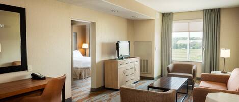 A hotel room with a bed, a desk with a telephone, a television, a coffee table, and two sofas.