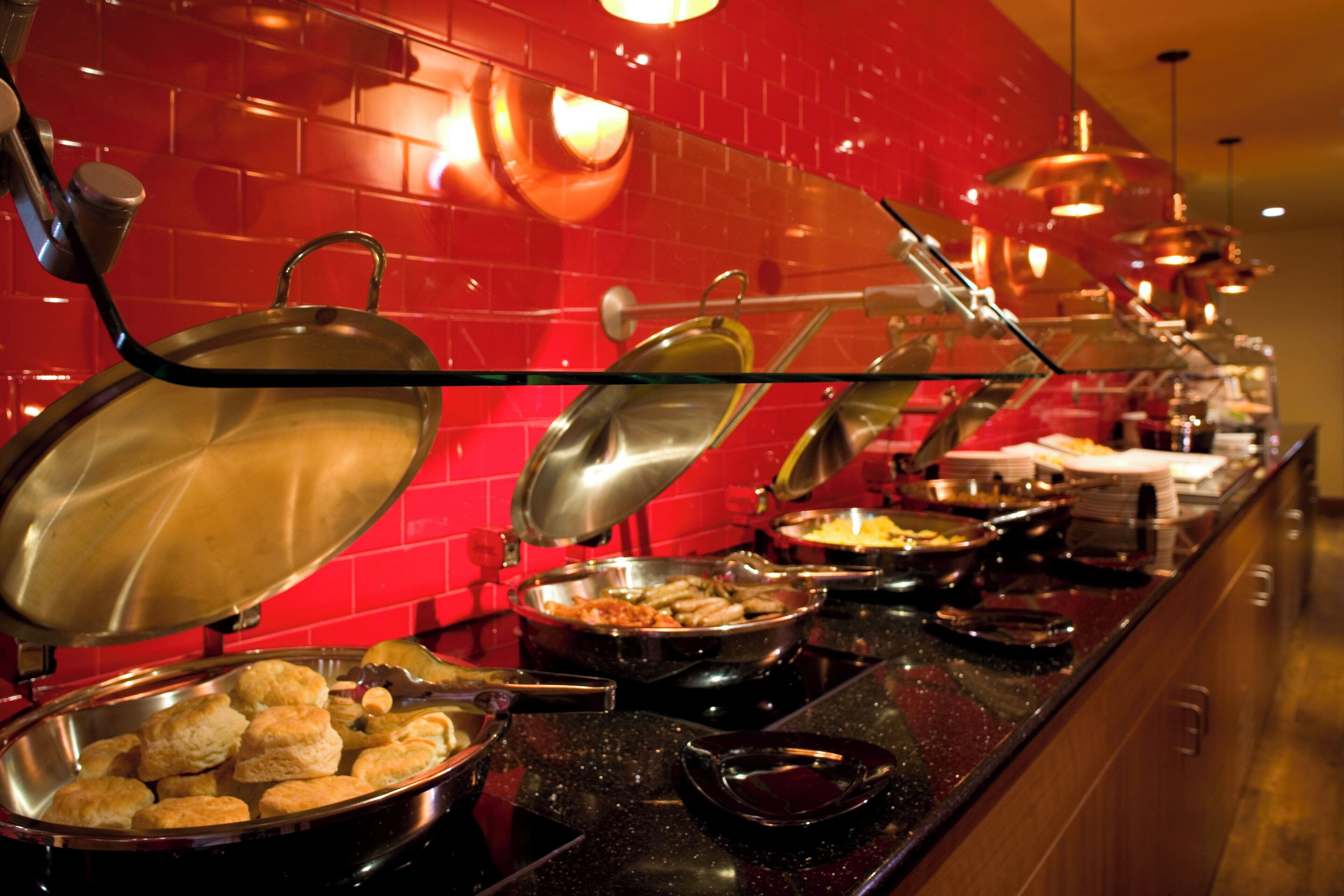 A buffet with various dishes and a red tiled wall.