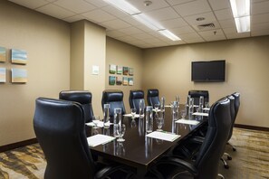 Un salón de conferencias con una larga mesa, sillas de cuero negro y un televisor de pantalla plana montado en la pared.