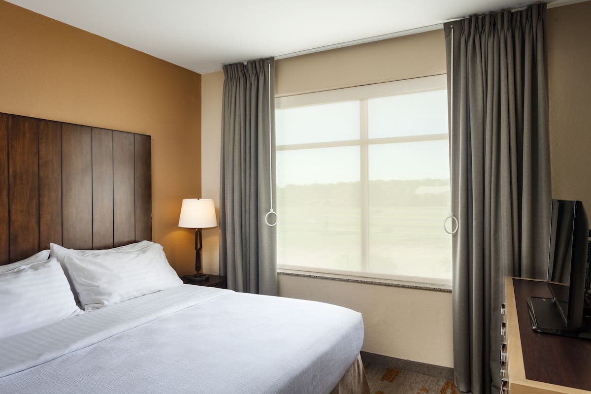 A hotel room with a bed, a desk with a computer, a lamp, and a window with curtains.