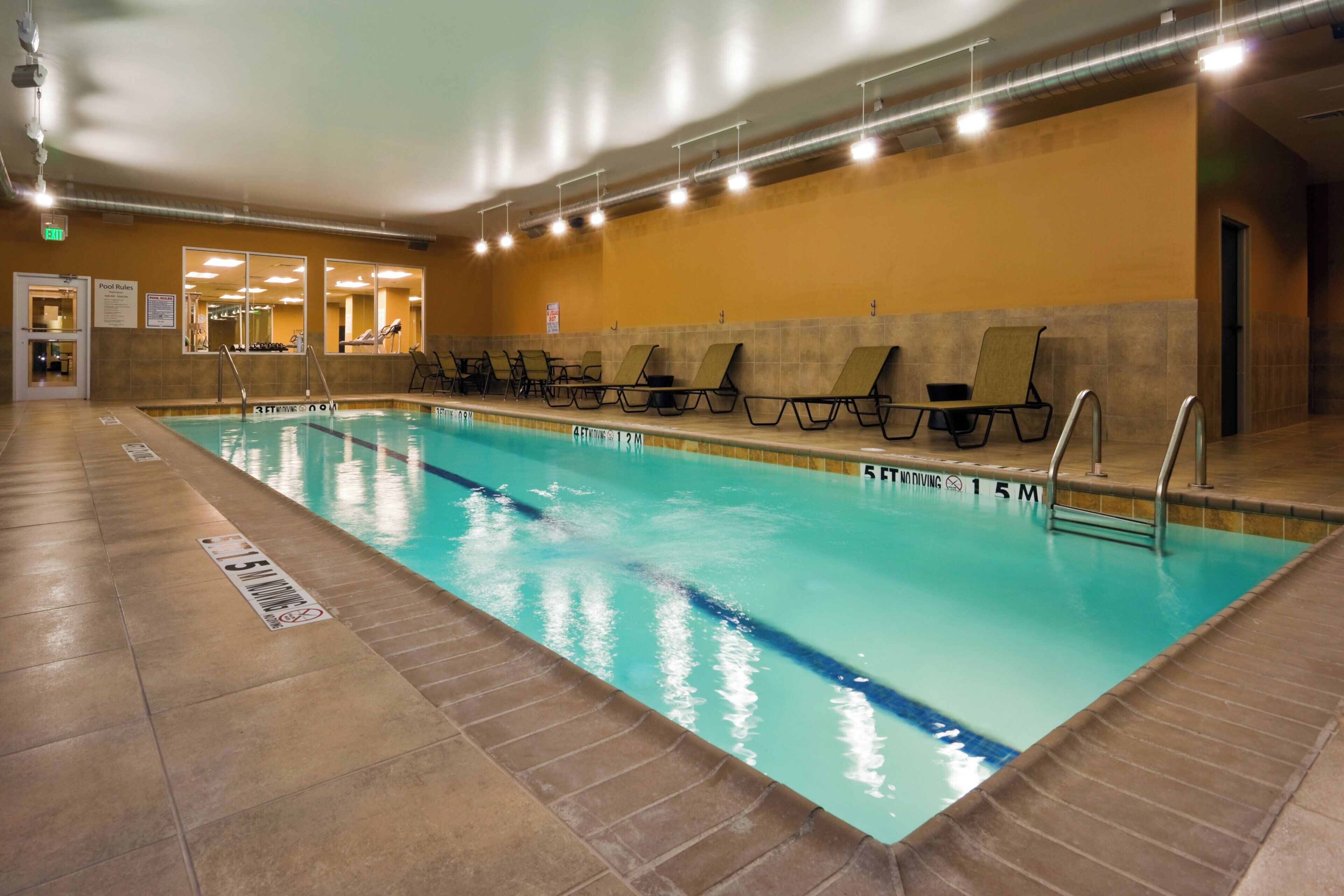 Piscina interna com faixas delimitadoras, cadeiras de descanso e piso revestido de azulejos.