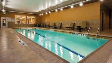 An indoor swimming pool with clear lane markings, lounge chairs, and a tiled floor.